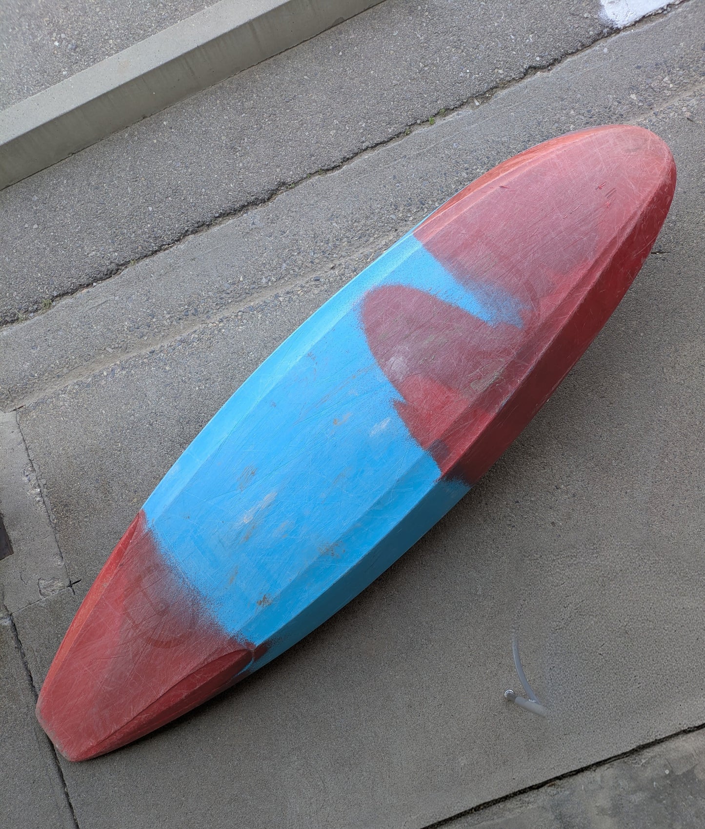 A Consignment Medium Ozone from 4Corners Riversports, with faded red and blue paint, lies upside down on concrete near steps, capturing the adventurous spirit of slicey river running.