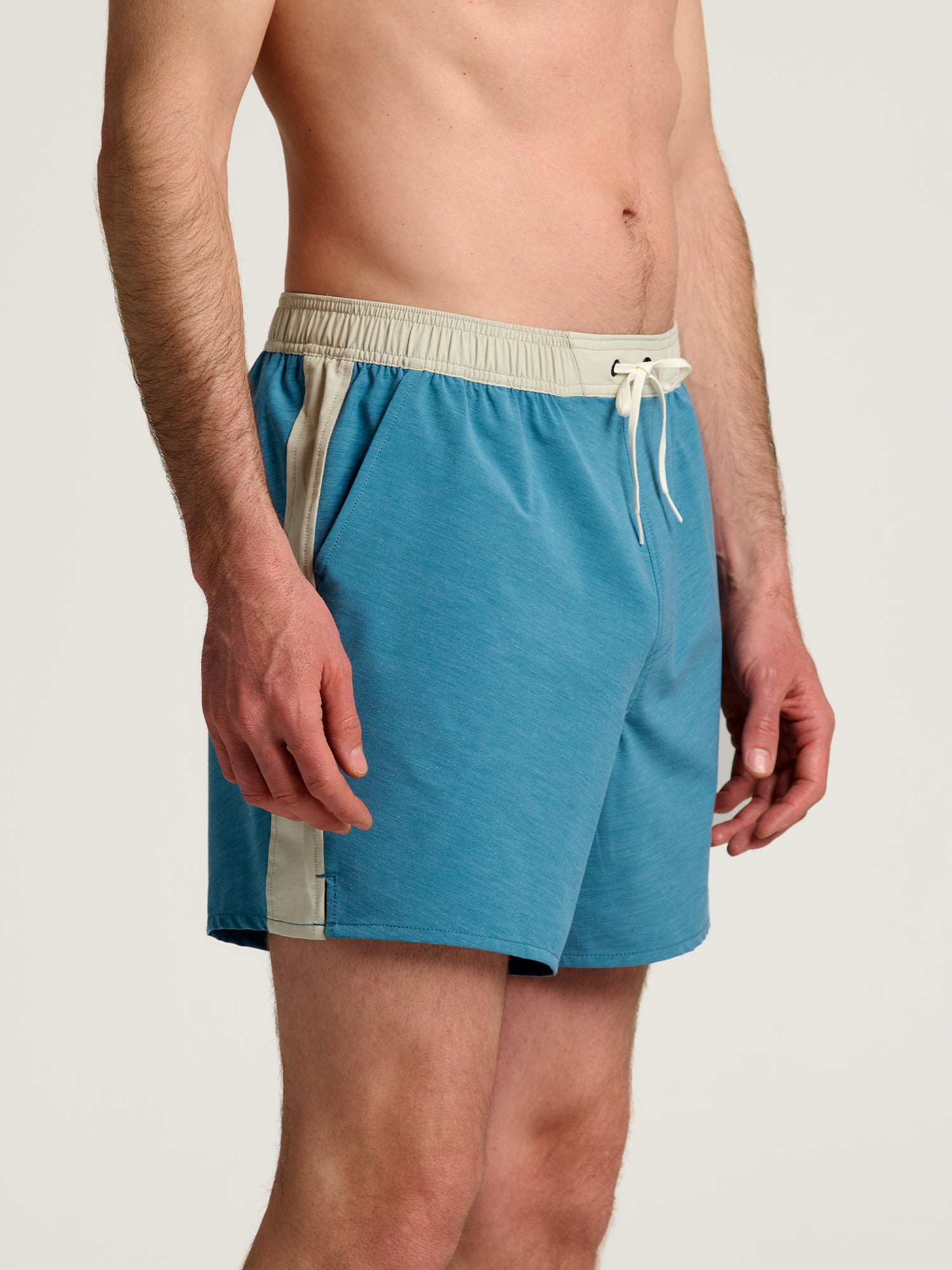 A man wearing Free Fly Palmera Boardshorts M's in teal with beige side stripes and waistband, made of quick-dry fabric by Free Fly, stands against a plain background.