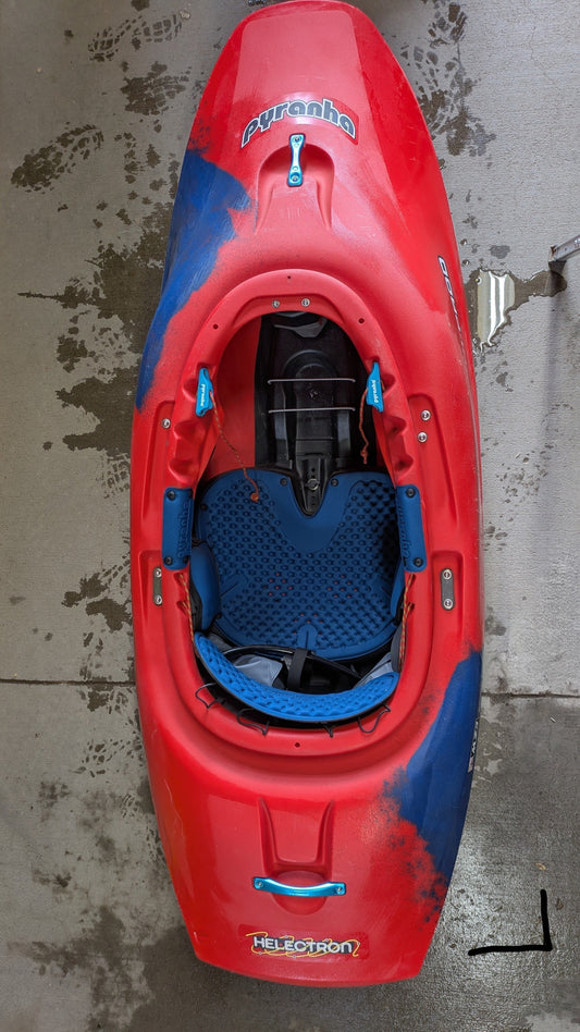 A Pyranha Demo Helectron kayak in red and blue from our demo fleet stands upright on a wet concrete surface.