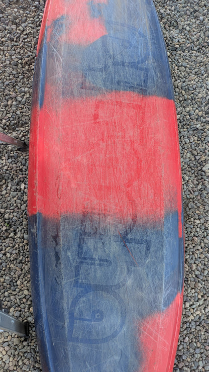 A scratched and worn red and black Pyranha Demo ReactR LG kayak rests on small gravel stones.