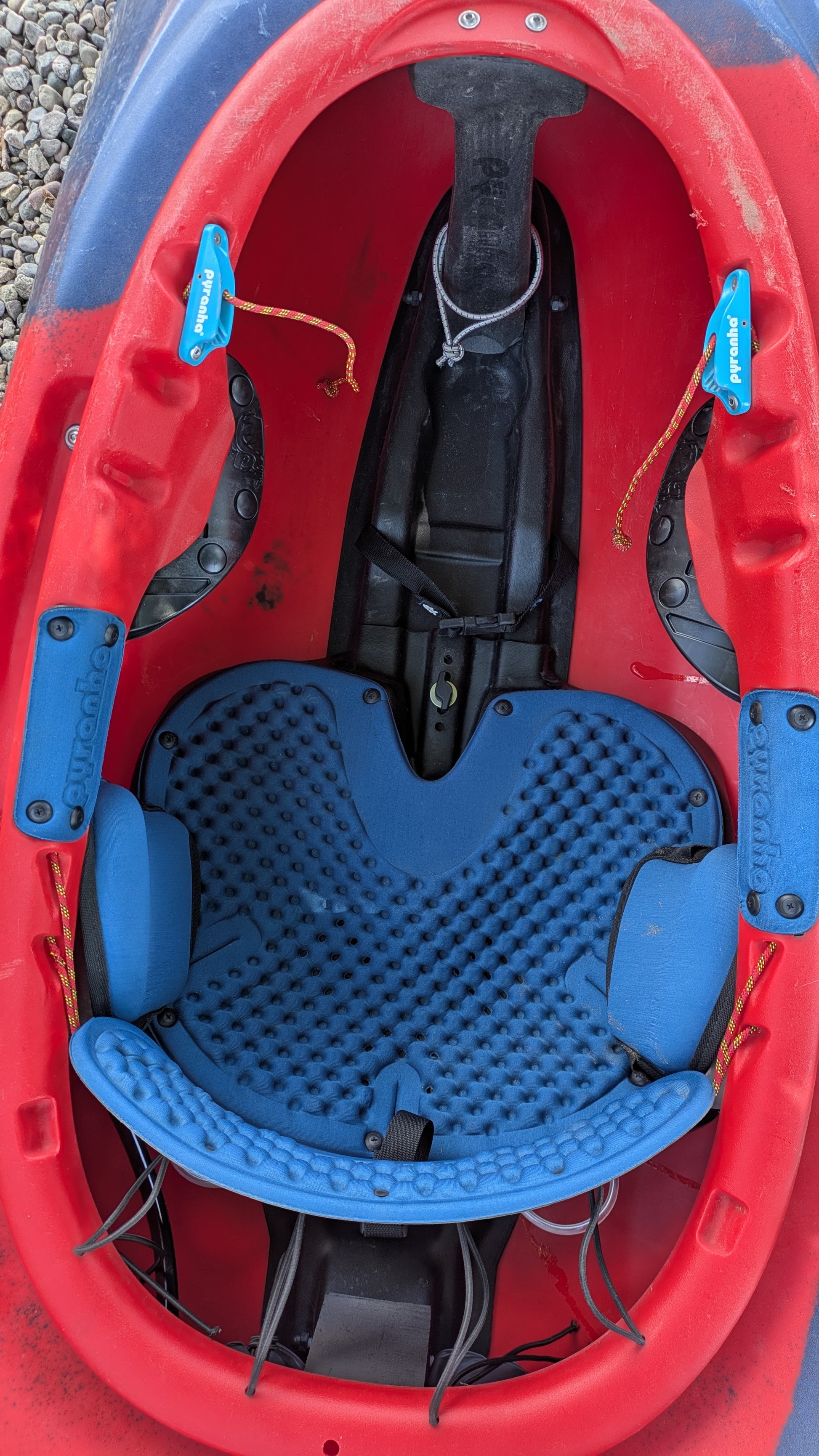 Top-down view of the cockpit of a Pyranha Demo ReactR LG boat in red and blue, featuring a padded blue seat, foot rests, and safety straps.