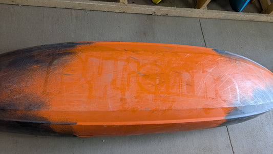 The underside of a used Pyranha Demo Scorch LG kayak, revealing scratches and worn paint patches, rests on a concrete floor.
