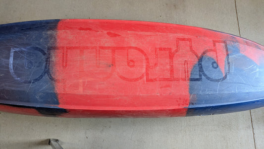 A used Pyranha Demo Scorch X kayak, red and blue with a partially visible upside-down "Outworld" logo on the bottom. Shows scratches from prior use—could have been a demo boat.
