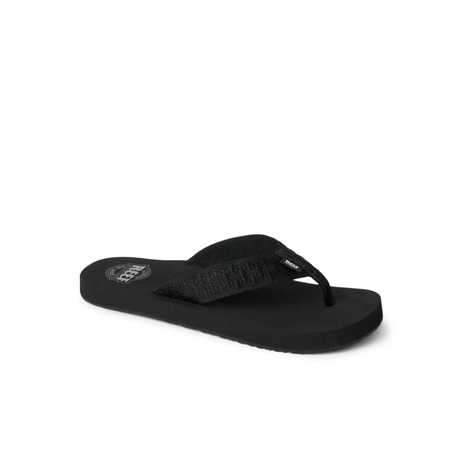 The REEF Smoothy Flip is a black flip-flop sandal with a textured strap and flat sole, offering cushy footbed comfort. Displayed on a plain white background.