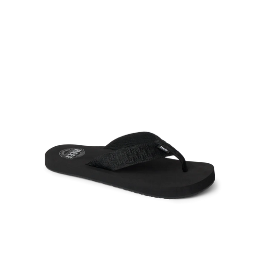 The REEF Smoothy Flip is a black flip-flop sandal with a textured strap and flat sole, offering cushy footbed comfort. Displayed on a plain white background.