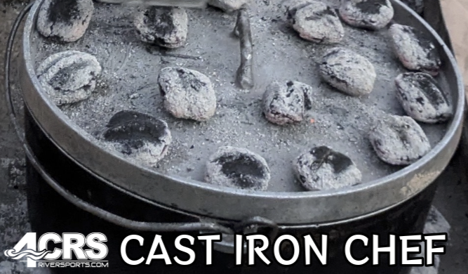 A 4CRS Cast Iron Chef pot with a lid, covered in round charcoal briquettes, ideal for riverside outdoor cooking.