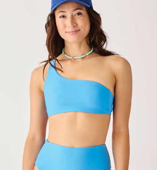 A woman wears the Carve Bondi Compression Top and matching bikini bottoms, paired with a blue cap and a beaded necklace, standing against a plain background.