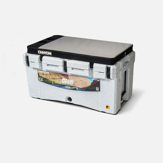 A rectangular gray portable cooler lid branded with "Canyon Coolers" features a printed image and silicone cup holders for convenience.