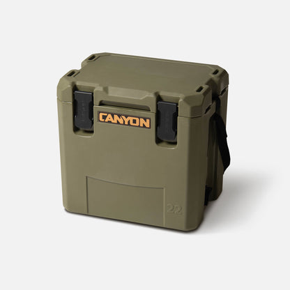 The Canyon Coolers Outfitter 22 V2 Cooler in green is a 22-quart rotomolded cooler with a black carrying handle and two black front latches, ideal for day trips. Shown on a plain white background.