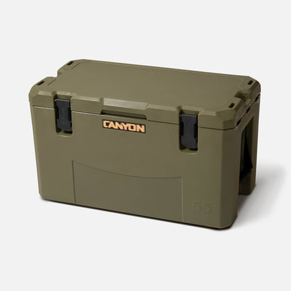 A large olive green Canyon Coolers Outfitter V2 Series Cooler with black latches and a front "CANYON" logo, featuring a dual action drain, is displayed against a plain white background.