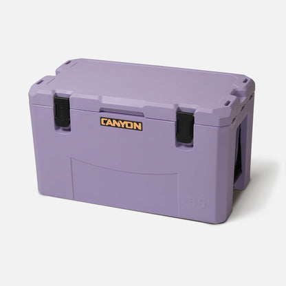 A rectangular, purple Canyon Coolers Outfitter V2 Series cooler with hinged lid, black latches, dual action drain, and “55” on the corner is shown against a white background. This premium cooler offers durable performance.