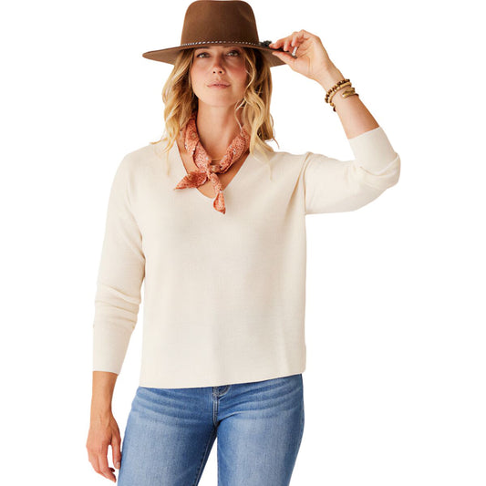 A person in the Carve Zella Merino Sweater stands against a white background, styled with a brown wide-brim hat, blue jeans, and a red patterned neck scarf.