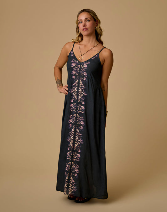A woman models the Carve Jordy Slip Dress, a black maxi with a pink and beige tie-dye center stripe, standing against a plain beige background.