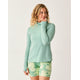 A woman wears the Carve Alani Sunshirt in light green with green floral shorts, standing against a plain background and smiling to the side.