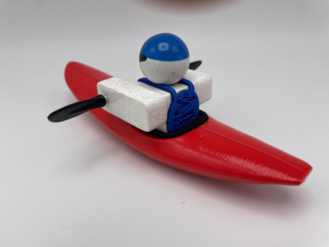 The Foamie Mini Creeker from the Foamie Friends collection features a toy figure in a red canoe with paddles, donning a blue helmet, set for river play against a simple backdrop.