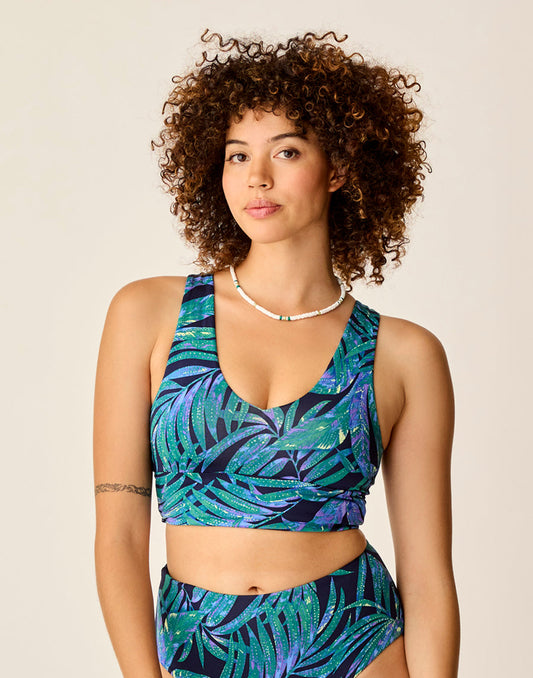 A woman with curly hair wears the eco-friendly Carve Tofino Top by Carve, featuring a leaf print and matching bottoms, standing against a neutral background.