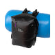 A black waterproof River Station Gear Dry Thwart Bag - V2 backpack with a purple zipper pull in front of a blue barrel.