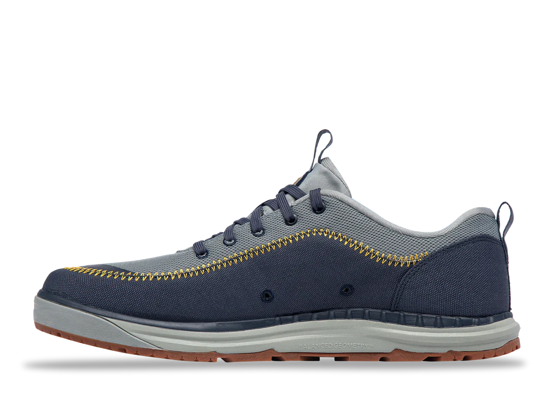 The Astral Brewer 3.0 features a side view of a blue and gray sneaker with yellow stitching, a gray sole, and brown tread. Made from hydrophobic canvas, it serves as a stylish yet functional water shoe.
