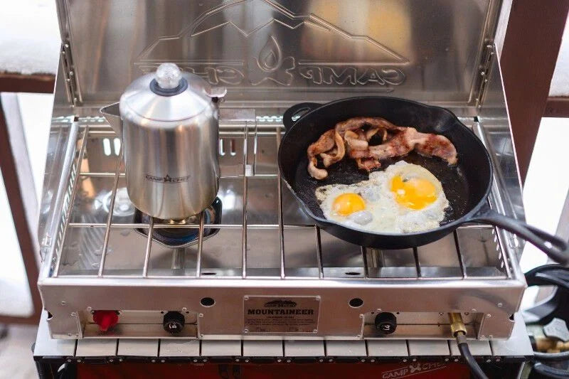 A Mountaineer Camp Stove by Camp Chef with a frying pan cooking eggs on it.