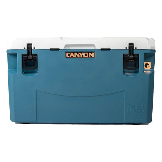 The blue and white PRO Series Cooler by Canyon Coolers, featuring black latches and a Route 66 logo, offers maximum ice retention and comes with a lifetime warranty, ensuring endless adventure.