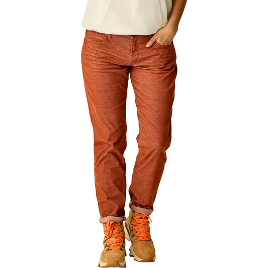 Wearing Carve's Carson Cord rust-colored pants, tan sneakers with orange laces, and a white top, this person stands casually with one hand in their pocket, channeling effortless skater girl style.