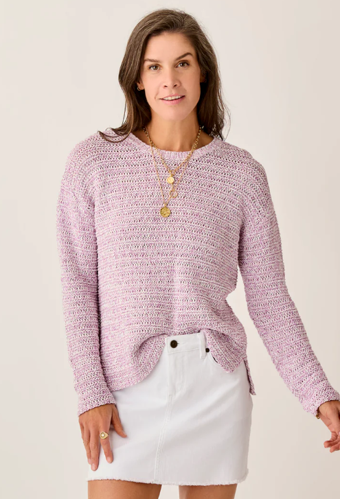 A woman wears the Carve Clarissa Marled Sweater in lavender, paired with a white mini skirt and layered gold necklaces, standing against a plain light background.