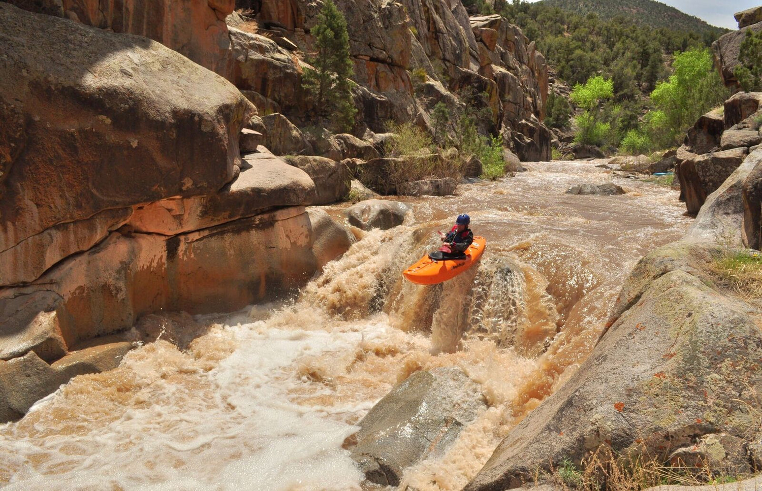a man riding a kayak down a river surrounded by rocks.