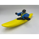 A Foamie Creeker from the Foamie Friends brand expertly maneuvers a yellow banana-shaped boat with bright blue paddles, capturing a playful river adventure against a simple backdrop.