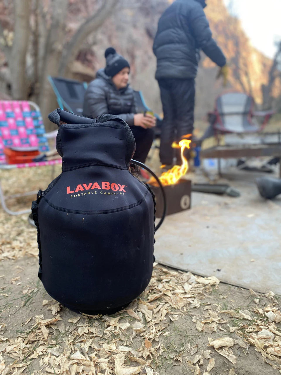 A man is sitting by a campfire with a LavaBox Propane Tank Top on his back.