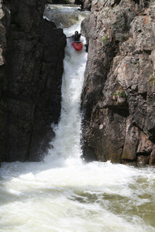 a man riding a kayak down a river next to a rocky cliff.