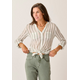 A woman in the Carve Dylan Gauze Tunic tied at the waist and sage green jeans stands with hands on hips against a plain background.