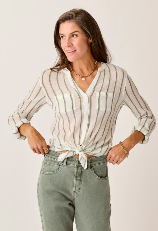 A woman in the Carve Dylan Gauze Tunic tied at the waist and sage green jeans stands with hands on hips against a plain background.