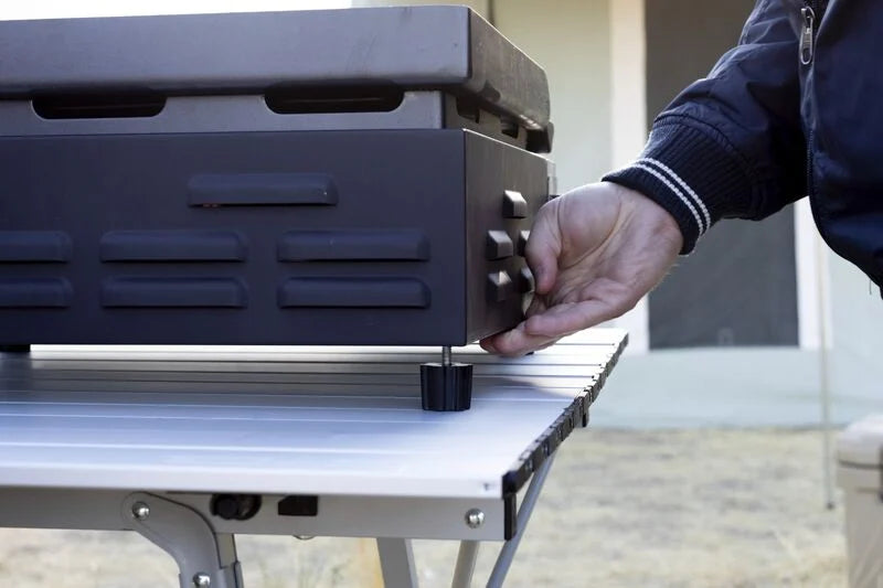 A man is placing a Camp Chef VersaTop 14 Flat Top Camp Stove on the table.
