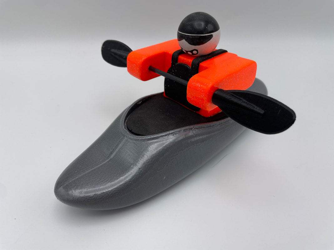The Foamie Play Boat by Foamie Friends includes a plastic toy kayak equipped with a Foamie Friends figure in an orange life vest, skillfully maneuvering river dynamics with a double paddle on its sleek gray design.