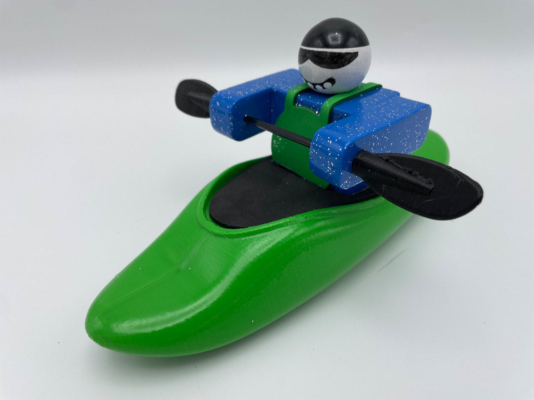 The Foamie Play Boat by Foamie Friends features a toy figurine expertly navigating river dynamics in a green kayak, equipped with blue arms, a black paddle, and finished with a helmet and sunglasses for the ultimate adventure vibe.