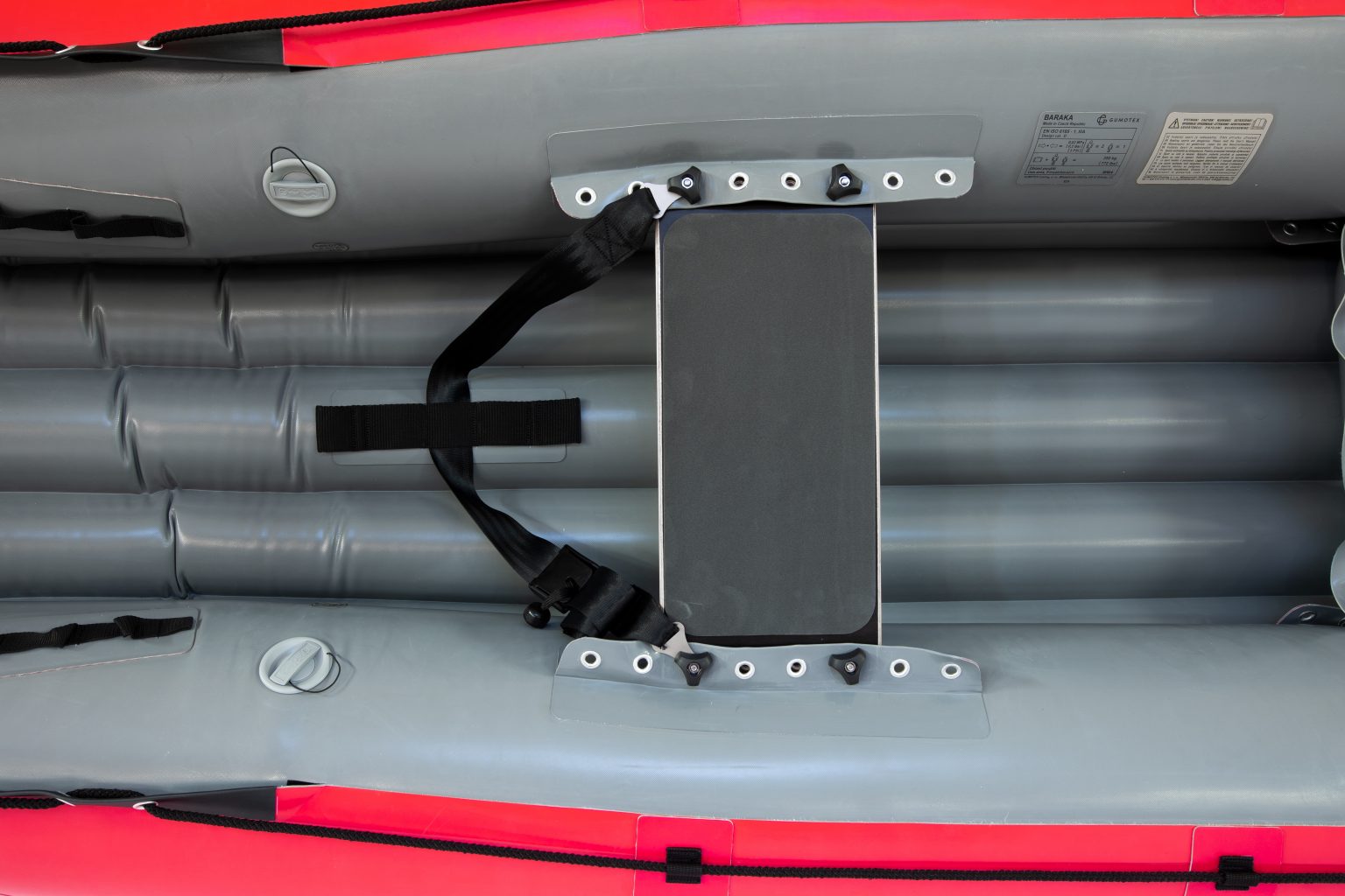 Top-down view of the interior of the Gumotex Baraka Inflatable Canoe, showcasing a red and gray design with a bench seat equipped with a black strap. This white water-ready vessel features a self-bailing bottom for added safety.