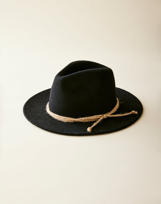 The Carve Alfred Hat is a black felt western hat featuring a rustic twine band around the base, shown on a light beige surface.