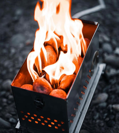 The LavaBox Hekla Portable Campfire / Stove Combo features large flames and hot stones in a stainless steel design, shown outdoors on a rocky surface.