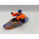 A Foamie Friends Swirl Play Foamie Boaters figure with a blue helmet and orange vest paddles in a blue and orange marbled plastic play boat against a plain light background.