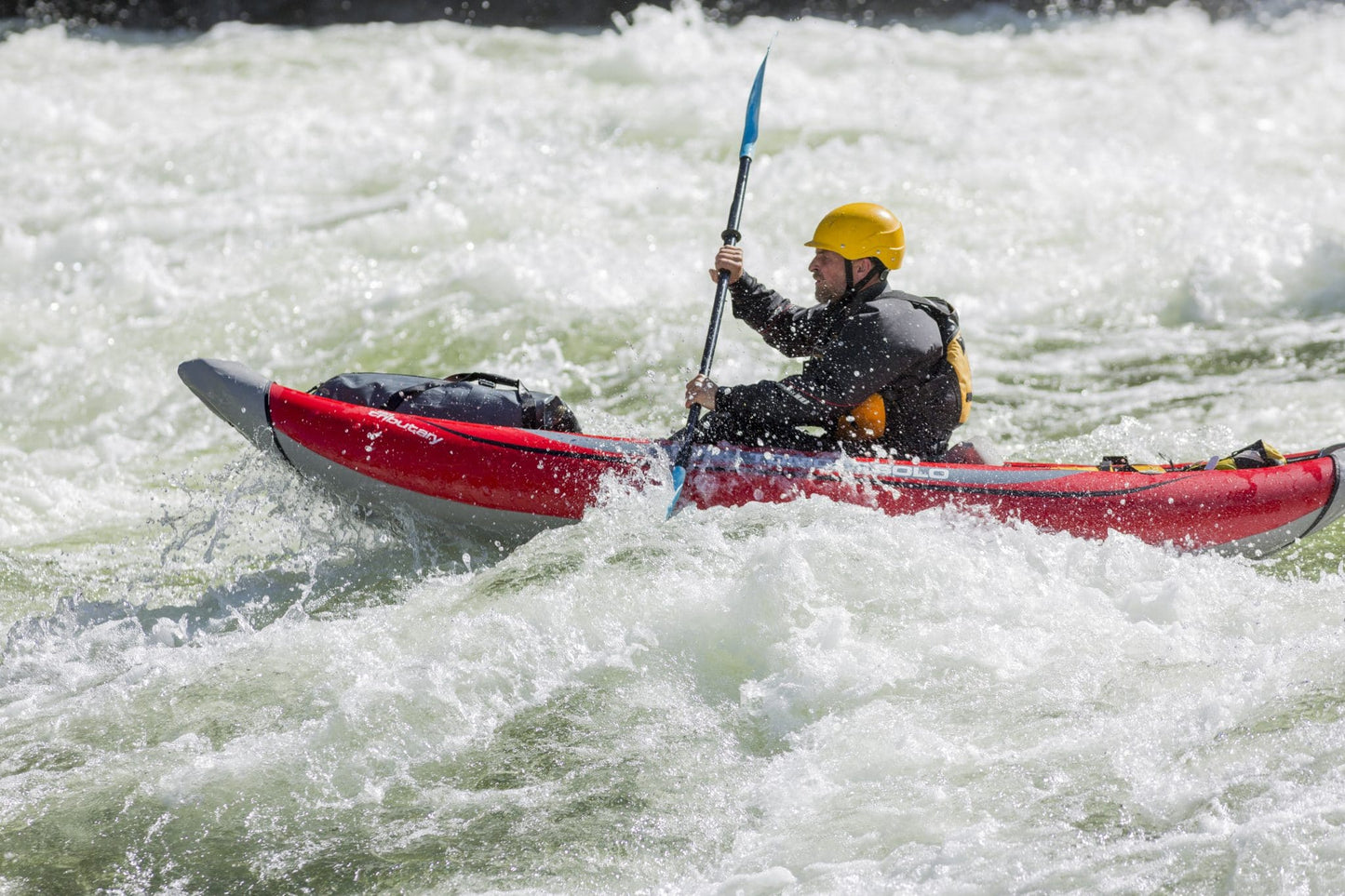 A person wearing a yellow helmet paddles a red 4CRS Rental Inflatable Kayak through whitewater rapids.