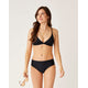 A woman wearing Carve's Pipa Compression Bottom stands against a plain background, looking to the side and holding sunglasses in her left hand.