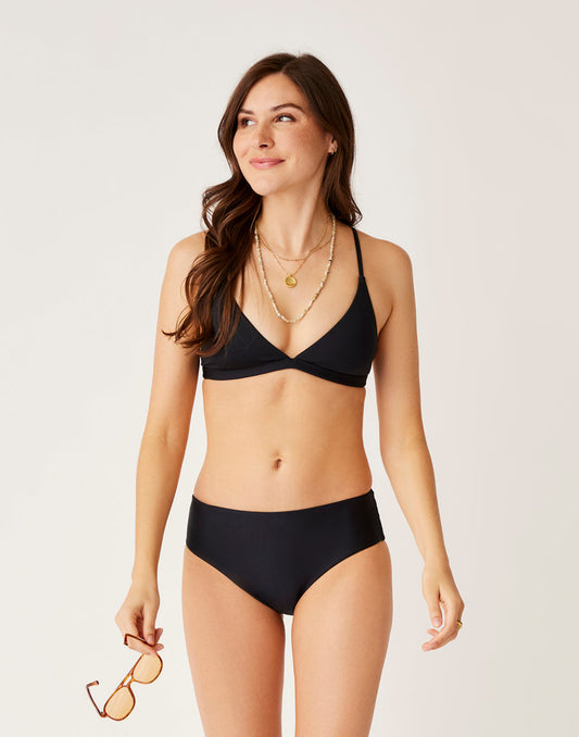 A woman models the Carve Pipa Compression Bottom in black, standing against a plain background, holding sunglasses in her left hand and gazing off to the side.