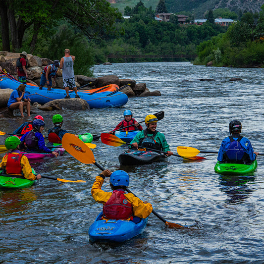 A group of people in Dirt + Paddle Lovers kayaks enjoying an outdoor adventure on a river.