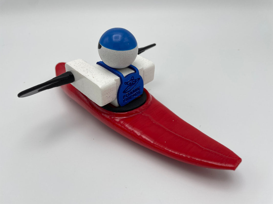 A small toy figure in a blue helmet and life vest sits in a Foamie Mini Slice kayak with black paddles, showcasing impressive hull design against a white background. This product is from the Foamie Friends brand.