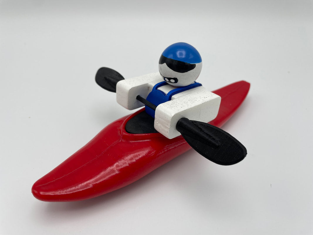 Foamie Friends' Foamie Mini Slice features a toy figurine in a red kayak with a blue helmet and black paddles, highlighting the sleek hull design of Mini Slice boats against a plain background.