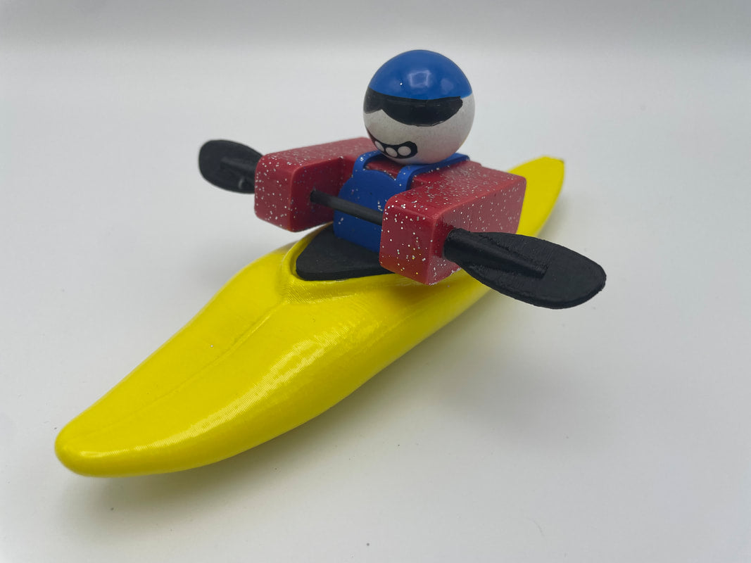 Toy figure from Foamie Friends of a person kayaking in a Foamie Mini Slice, featuring a sleek hull design with a yellow kayak, red arms, and a blue helmet.