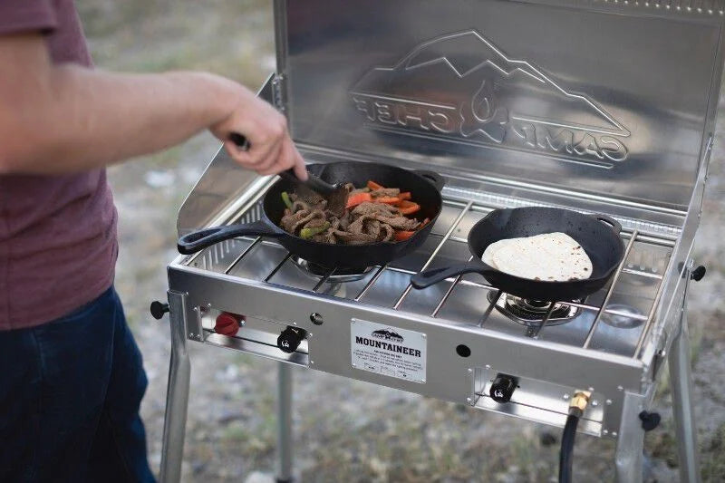 A mountaineer is preparing food on a Camp Chef Mountaineer Camp Stove in an outdoor kitchen.