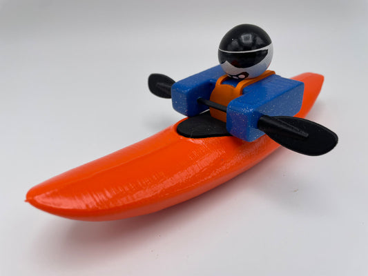 The Foamie Mini Creeker by Foamie Friends includes a plastic toy kayak accompanied by a figure sporting a black helmet and an orange life jacket, ideal for river play. Complete with black paddles, this adventurous companion is perfect for imaginative water adventures.