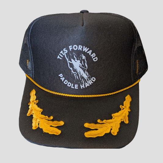 The EastWest 4CRS Tits Forward Paddle Hard is a black mesh polyester trucker hat with gold embroidered oak leaves, "TITS FORWARD PADDLE HARD" above a paddler graphic, and an adjustable Snapback closure for a comfy fit.