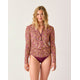 A woman faces forward against a plain background, wearing the Carve Cruz Rashguard with long sleeves and a floral print, paired with maroon bikini bottoms.
